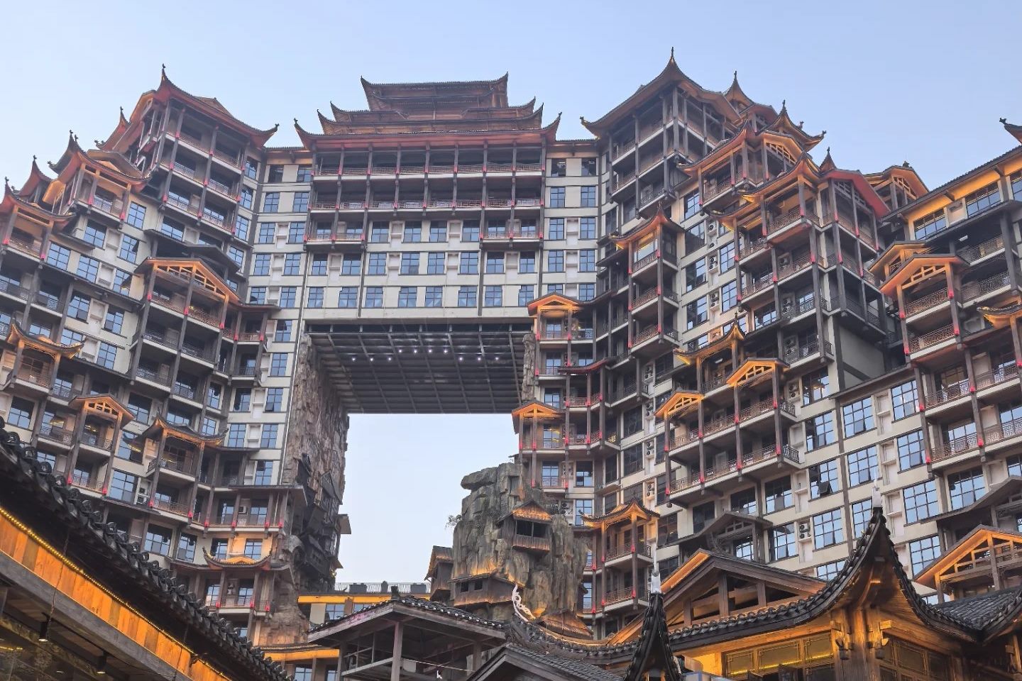 72 Qilou in Zhangjiajie by day, seen from the courtyard below: a huge multi-storey building dressed as a Tujia stilt house, with modern aluminium windows, air-conditioning units and concrete floor slabs visible behind the timber balconies.