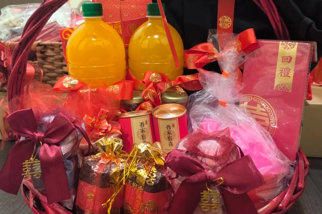 A red basket of return gifts: drinks, tea caddies marked with a happiness character, wrapped sweets, and a red box labelled 回禮