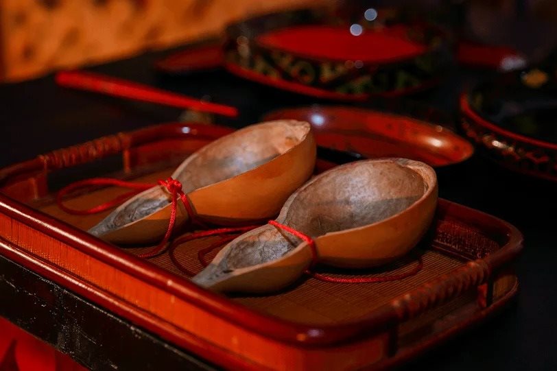 Two halves of a dried bottle gourd made into drinking ladles, joined by a red cord on a red lacquer tray