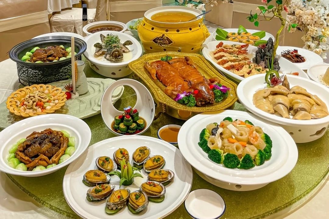 A wedding banquet table loaded with dishes including a whole roast bird, abalone, prawns and braised feet