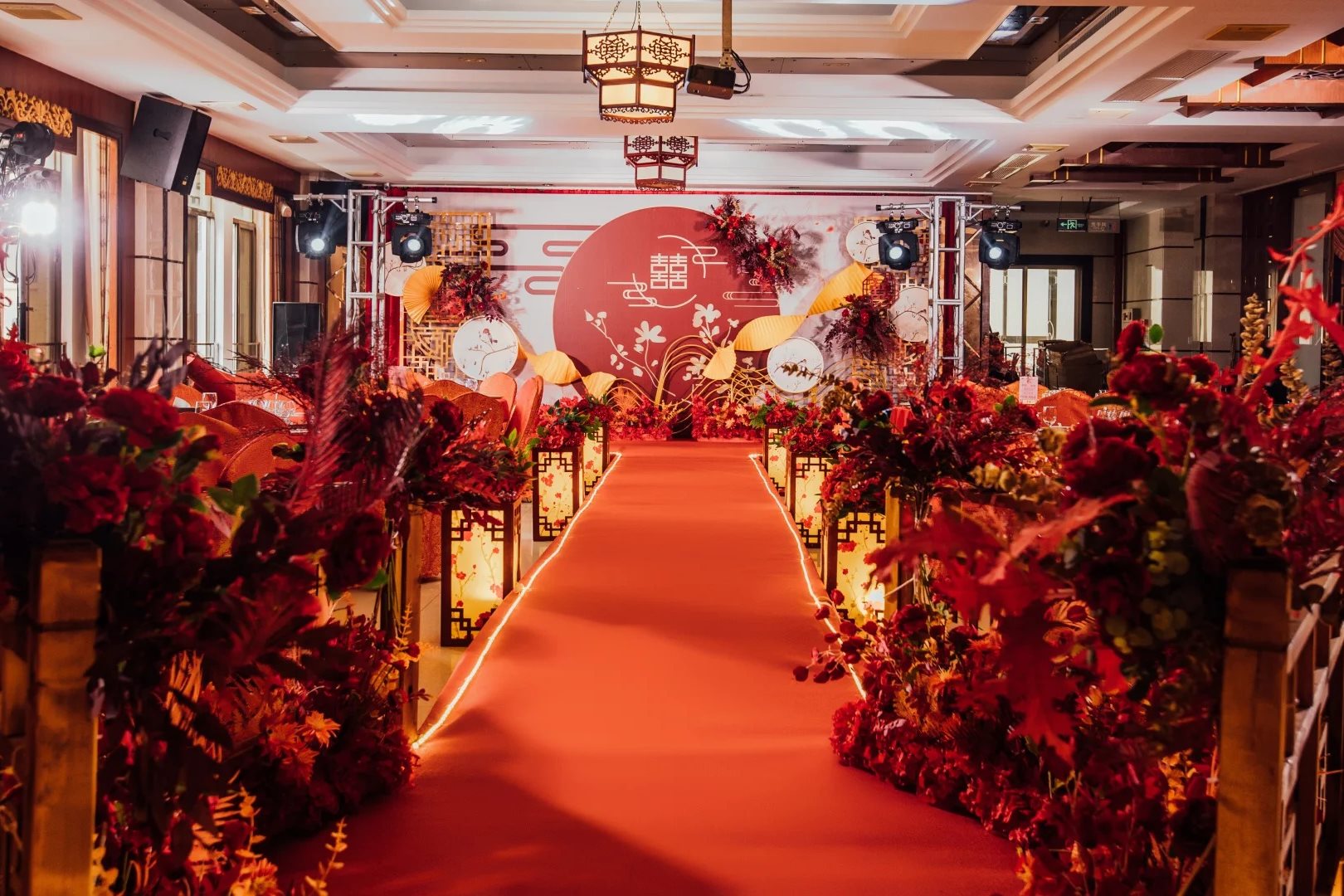 Chinese wedding ceremony aisle with a red carpet, double-happiness backdrop and lantern-lined floral arrangements