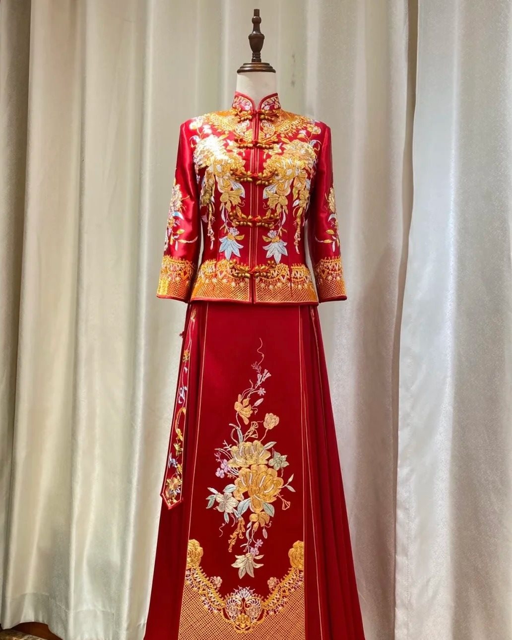 A red xiuhe wedding outfit on a dress form: a mandarin-collared jacket with a diagonal front closure over a pleated horse-face skirt