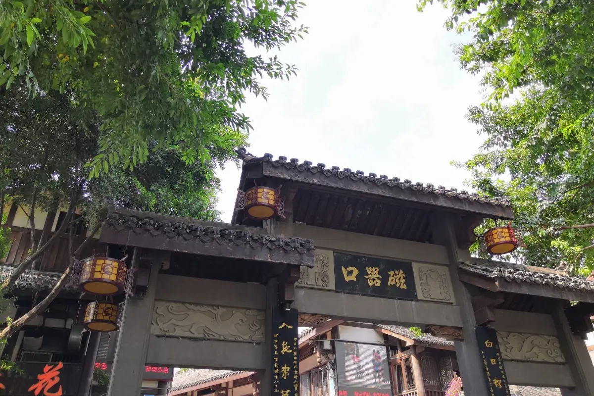 The Ciqikou Ancient Town entrance gate (paifang) with yellow lanterns and green trees, Chongqing.