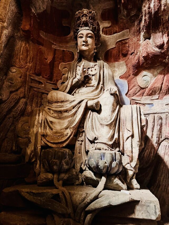 Seated bodhisattva carving on a lotus pedestal against a deep-red sandstone cliff at Dazu Rock Carvings, Chongqing.