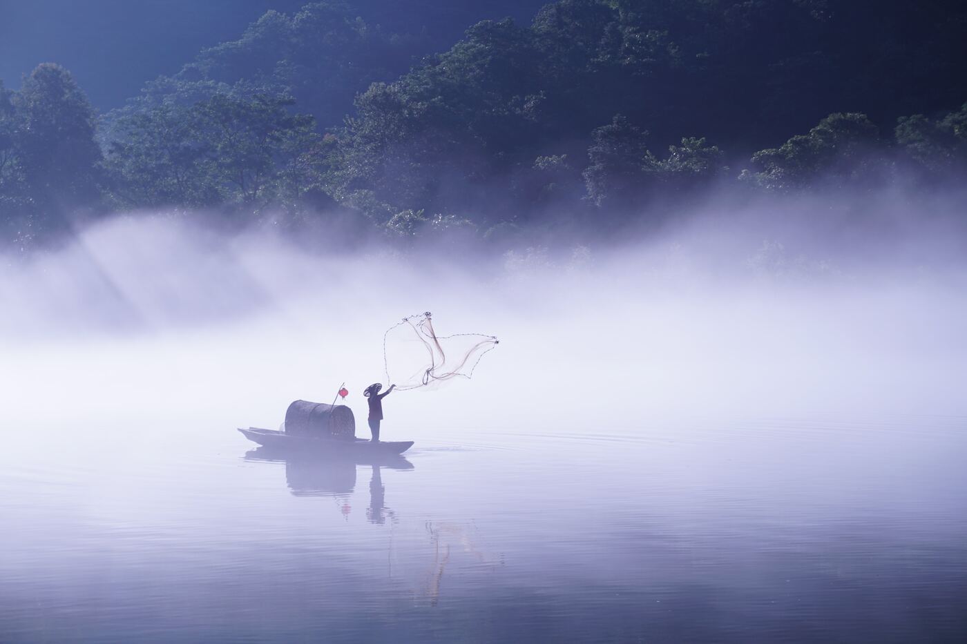 A lone fisherman casting a net from a boat on a misty stretch of the Li River below the karst peaks.