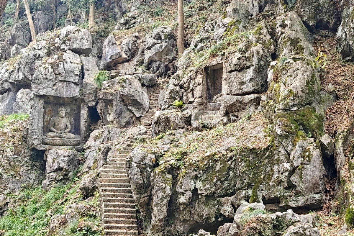 The limestone cliff at Feilai Feng, Hangzhou, with several carved Buddhist niches at different heights and a stone stairway climbing between them.