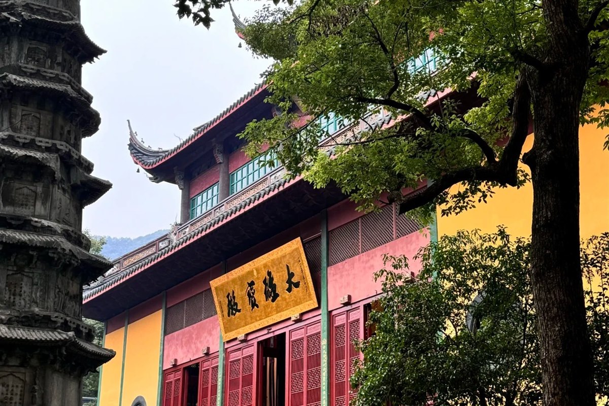 The Mahavira Hall at Lingyin Temple in Hangzhou — a gilded plaque reading 大雄寶殿 under three tiers of eaves, with one of the temple's carved Song-dynasty stone pagodas in the foreground.