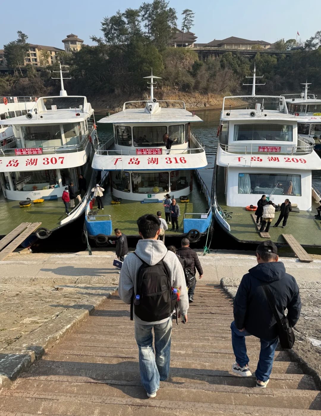 Passengers walking down stone steps towards three white double-deck cruise boats moored side by side at the Central Zone pier on Qiandao Lake