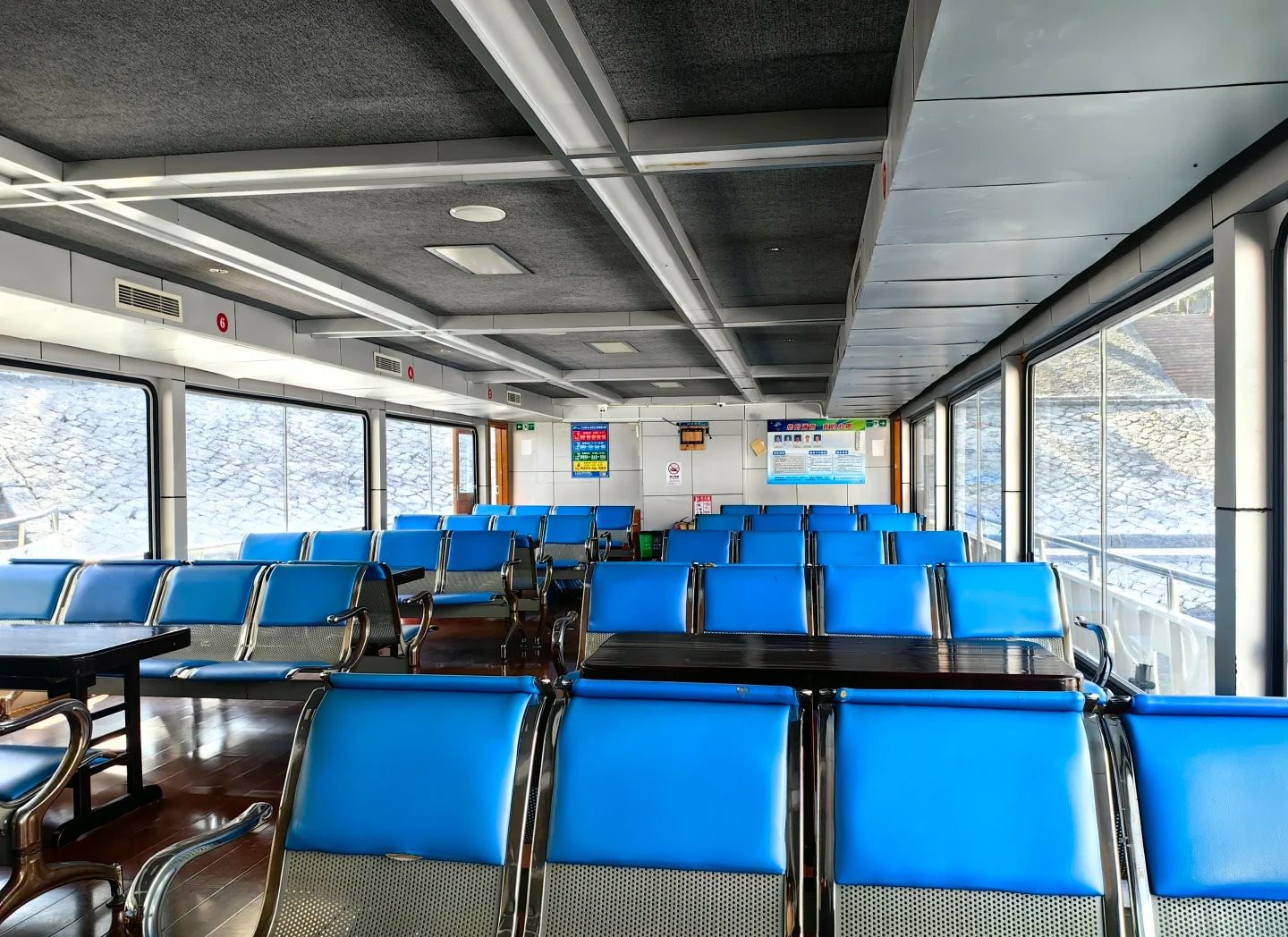 Rows of blue vinyl bench seats and wooden tables inside the passenger saloon of a Qiandao Lake cruise boat