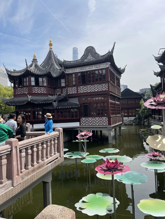 The curved-roof Huxinting teahouse building over the lake at Yuyuan Bazaar, with decorative lotus lily pads and visitors on the zigzag bridge.