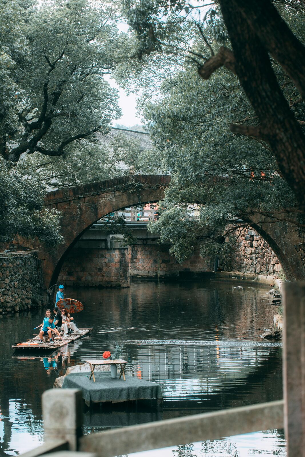 A stone arch bridge over a tree-shaded Suzhou canal, with a small boat on the water in the old town.