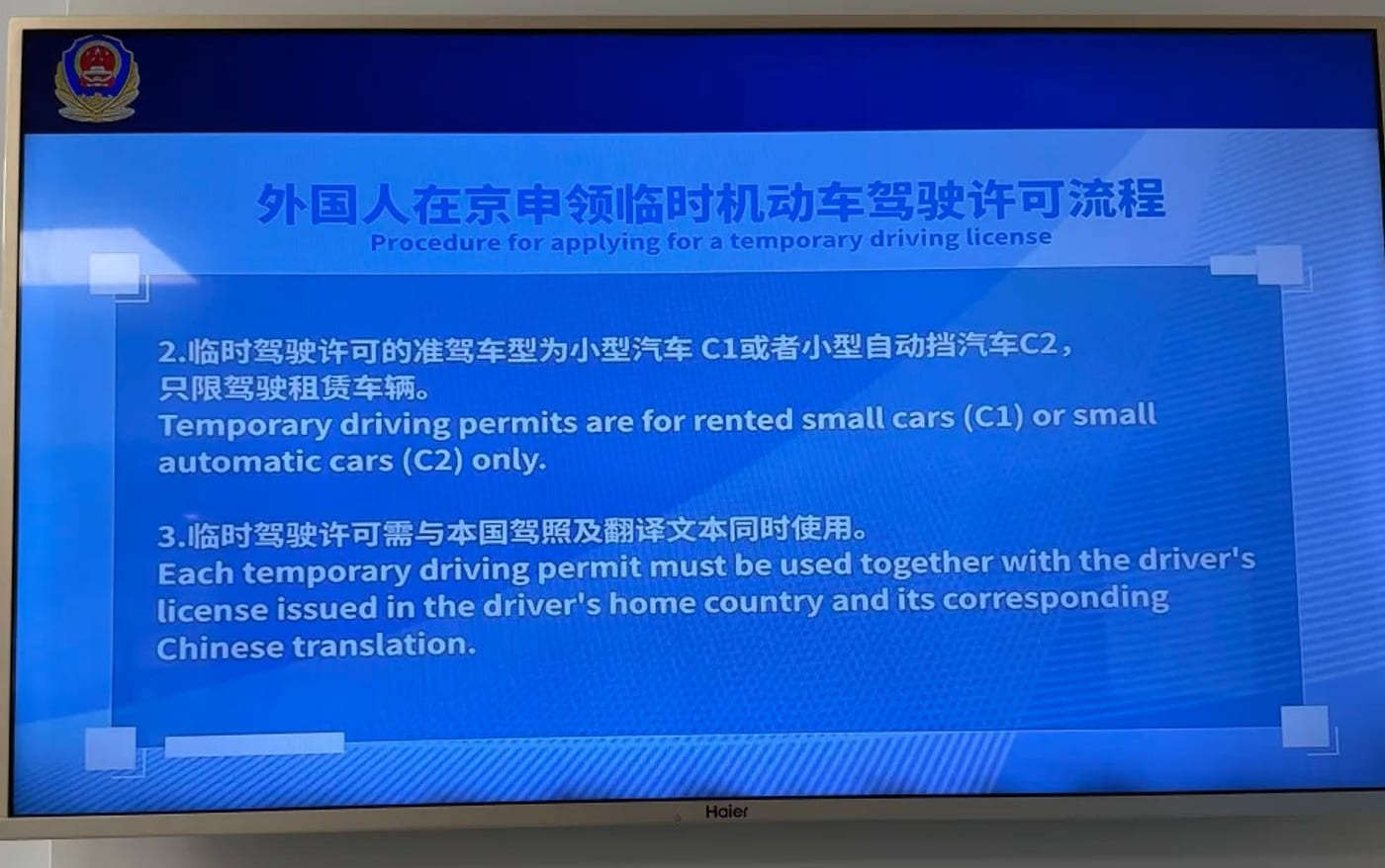 Police information screen at Beijing Daxing airport stating in Chinese and English that temporary driving permits are for rented small cars (C1) or small automatic cars (C2) only, and that each permit must be used together with the driver's home-country licence and its Chinese translation.