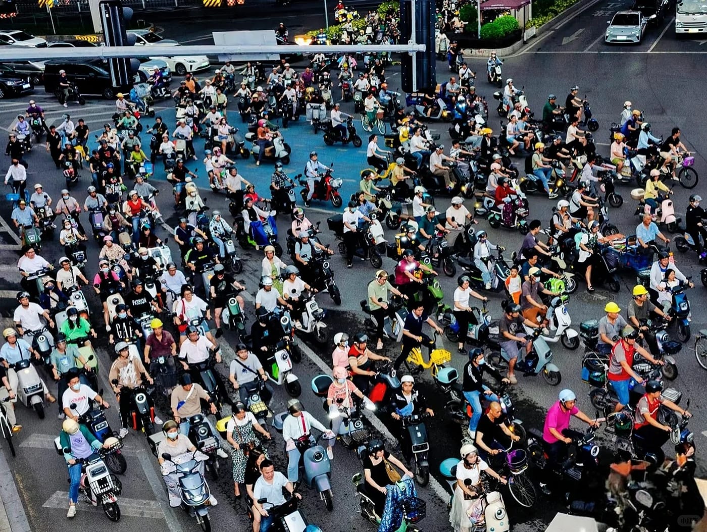A Shenzhen intersection seen from above, packed with several hundred electric scooters and bicycles waiting at the lights alongside cars.