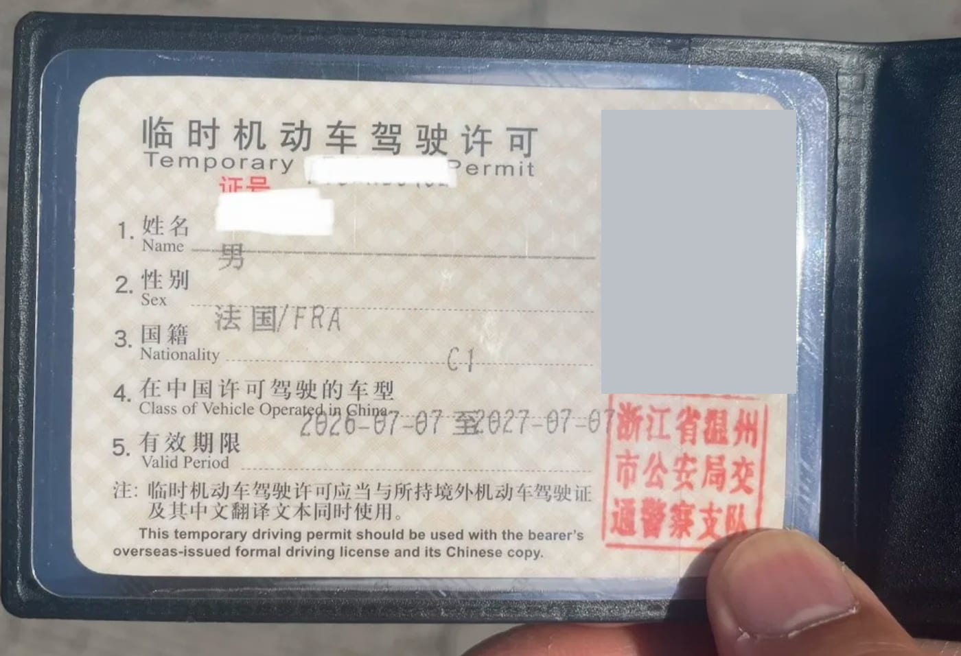 A Chinese temporary motor vehicle driving permit issued by the Wenzhou traffic police, showing nationality France, vehicle class C-1, and a validity period running from 7 July 2026 to 7 July 2027, with the holder's photograph and name redacted.