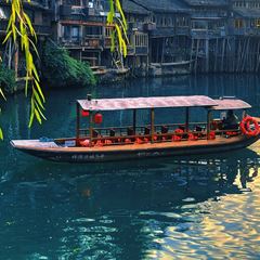 A wooden boat poling down the Tuojiang River in Fenghuang between stilt houses, boatman standing at the stern.