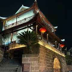 The East Gate tower of Fenghuang Ancient Town lit at night — a timber tower with upturned eaves above a stone gate arch in the old city wall.