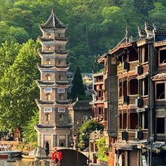 Wanming Pagoda standing slim on the bank of the Tuojiang River in Fenghuang, reflected in the water.