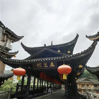 The Tuwang covered bridge of Furong Ancient Town, its dark timber roof and red lanterns above a stone plaza, the 土王桥 plaque visible.