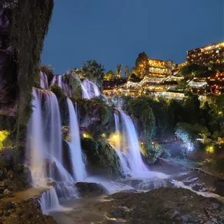 The Furong Ancient Town waterfall at night, lit and cascading in multiple strands below the illuminated old town.