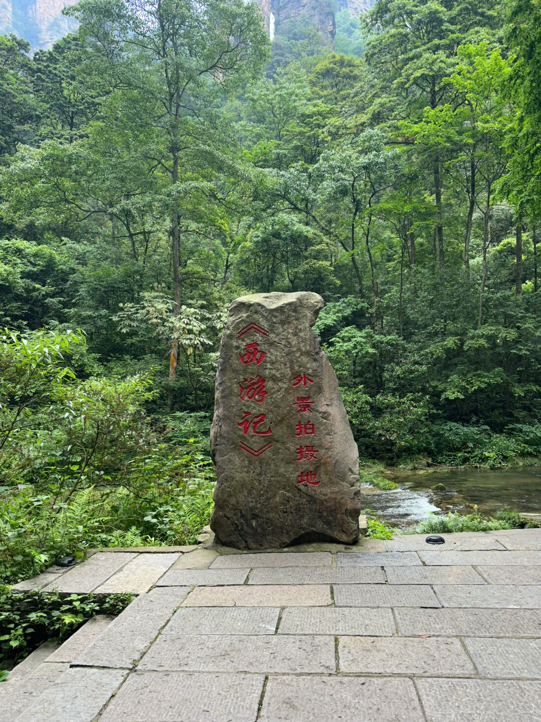 The carved stone marker beside the Golden Whip Stream trail reading 《西游记》外景拍摄地 — 'Journey to the West filming location' — with the forested valley behind.