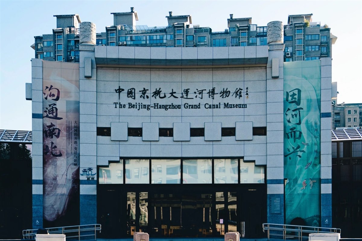 The symmetrical stone facade of the Beijing-Hangzhou Grand Canal Museum, its name in Chinese and English above the entrance, mirrored in the pool in front.