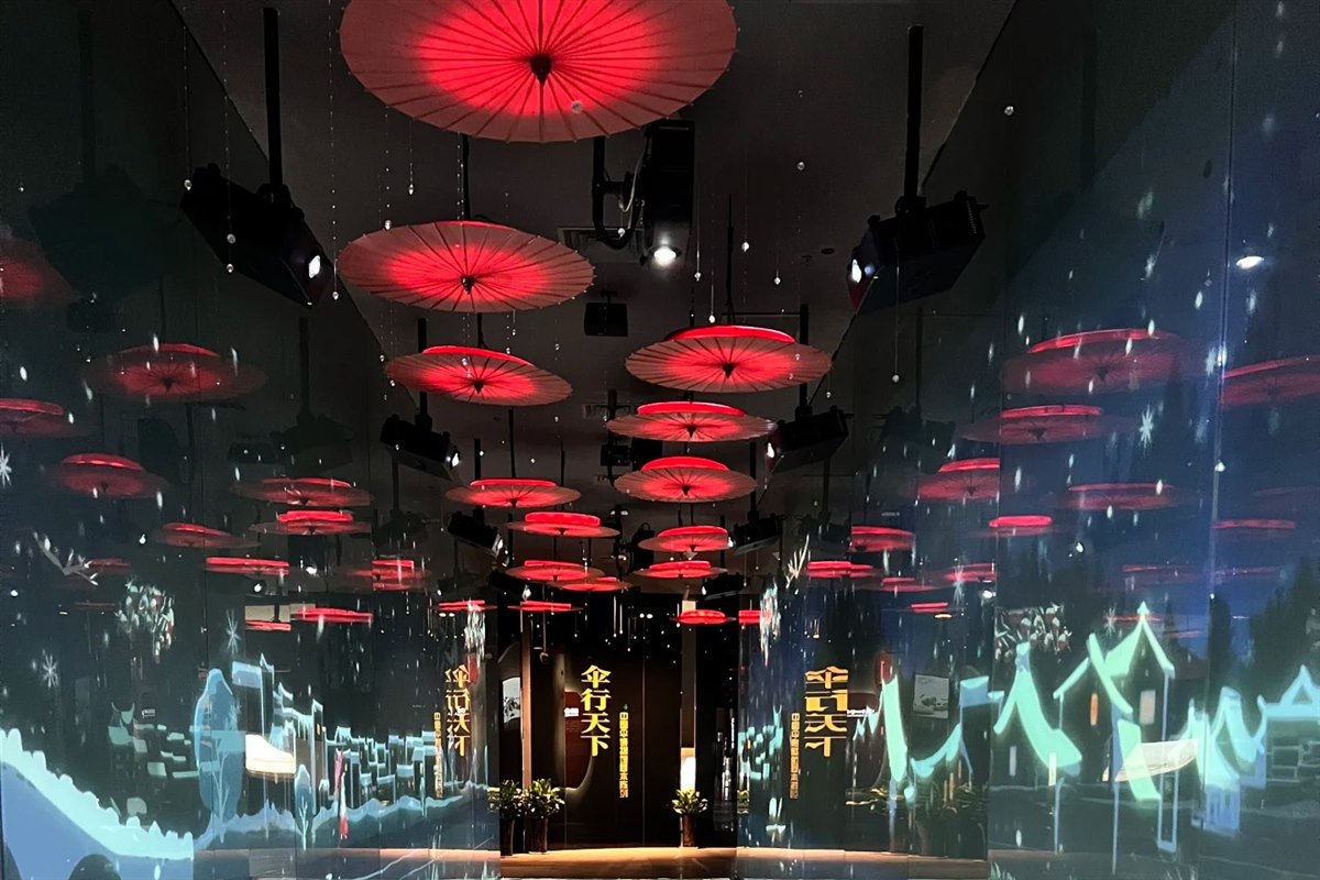 A mirrored corridor in the China Umbrella Museum, hung with rows of red oil-paper umbrellas that cast dappled shadows across the floor.