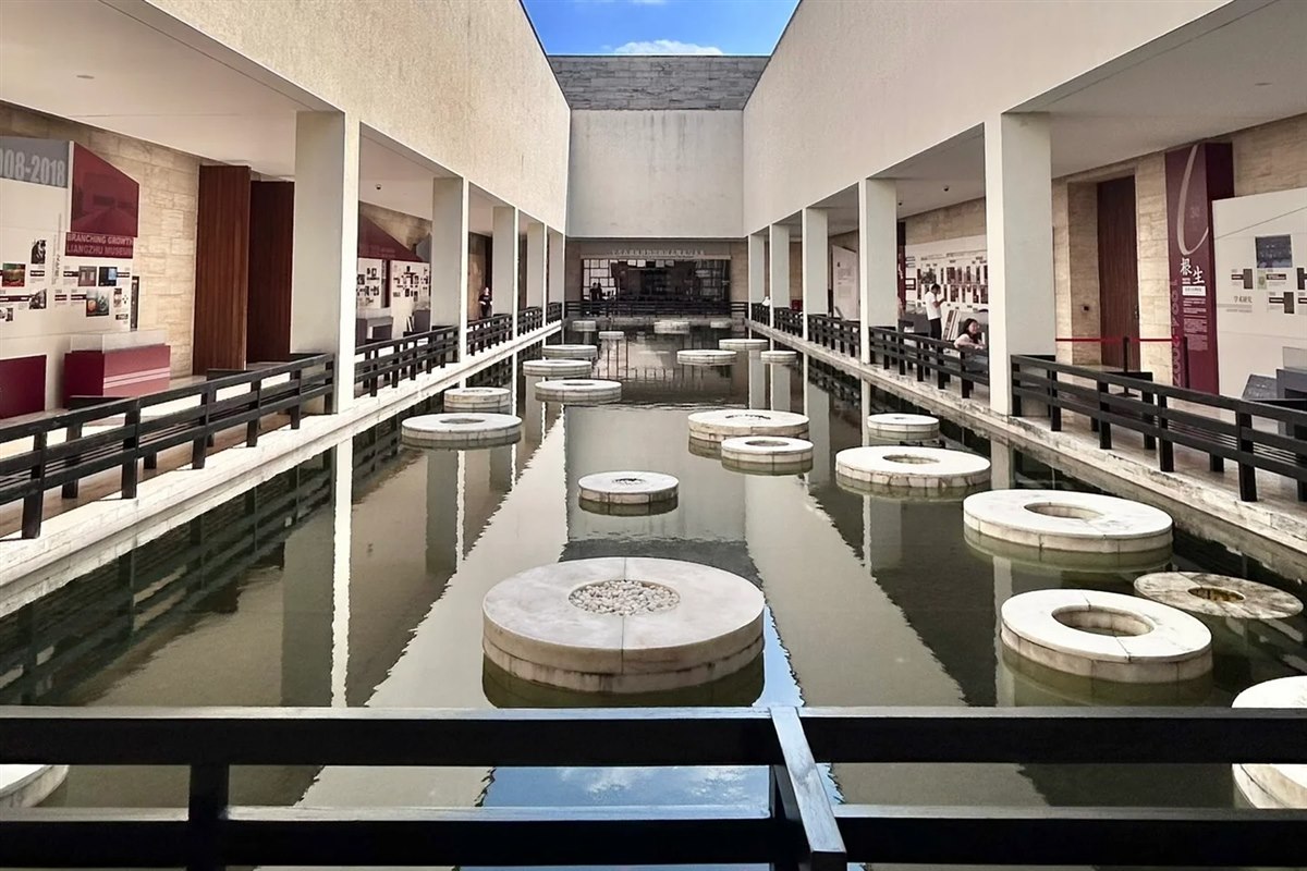 A long reflecting pool in a courtyard at Liangzhu Museum, flanked by stone-clad wings, with circular stone forms set in the water.