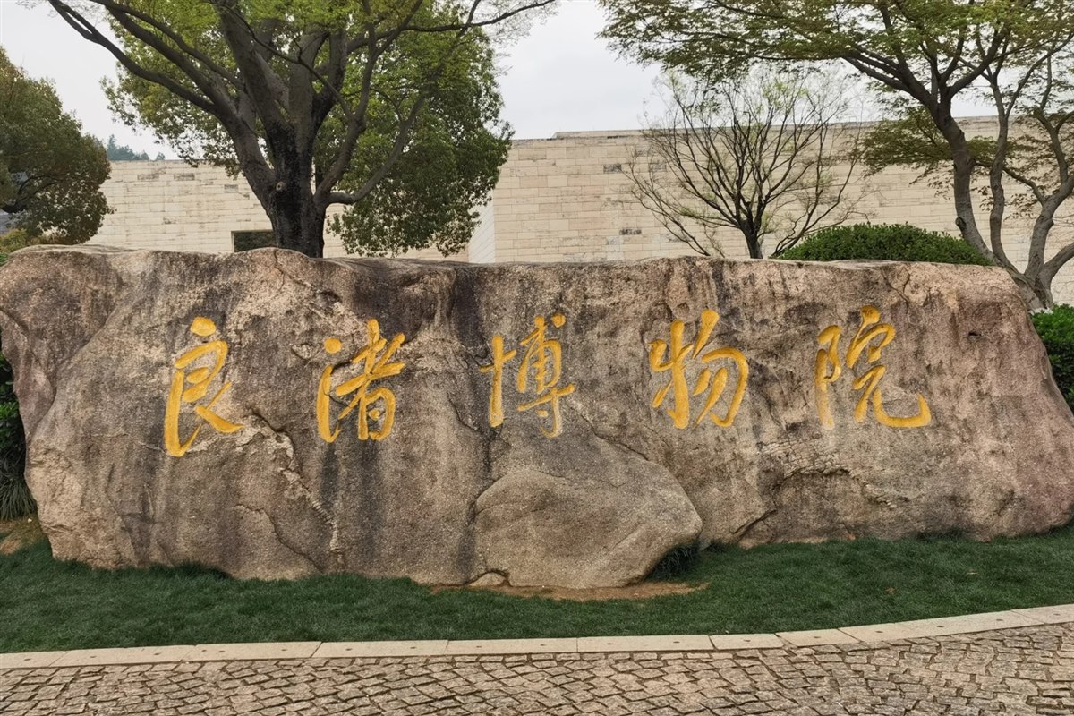 A large boulder outside Liangzhu Museum carved with the museum's name in gold characters, with the pale stone-clad building behind.