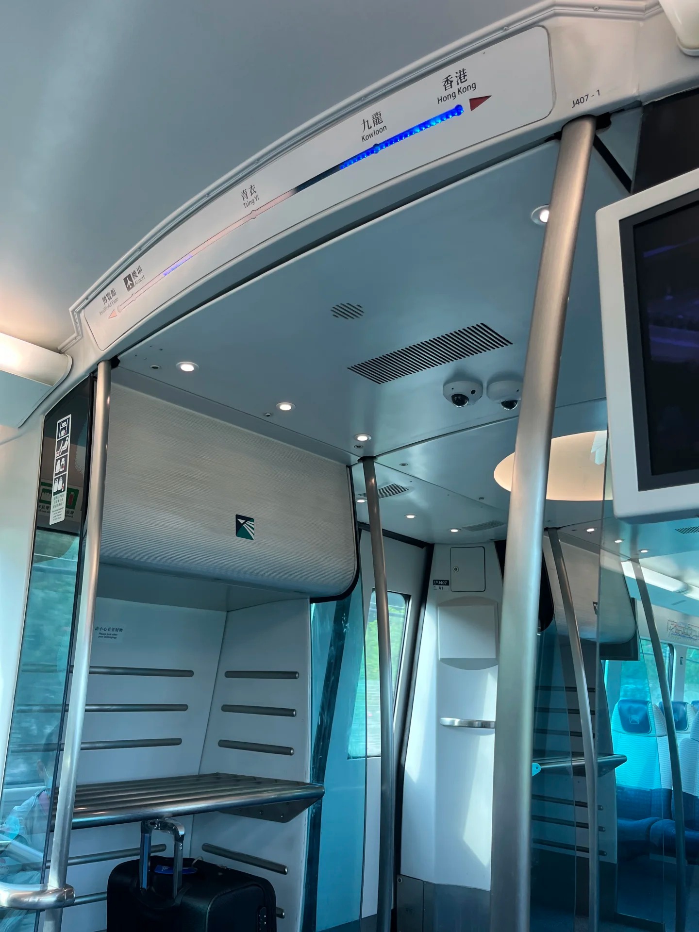 Inside an Airport Express carriage: the line diagram above the door showing AsiaWorld-Expo, Airport, Tsing Yi, Kowloon and Hong Kong stops, with luggage racks by the door