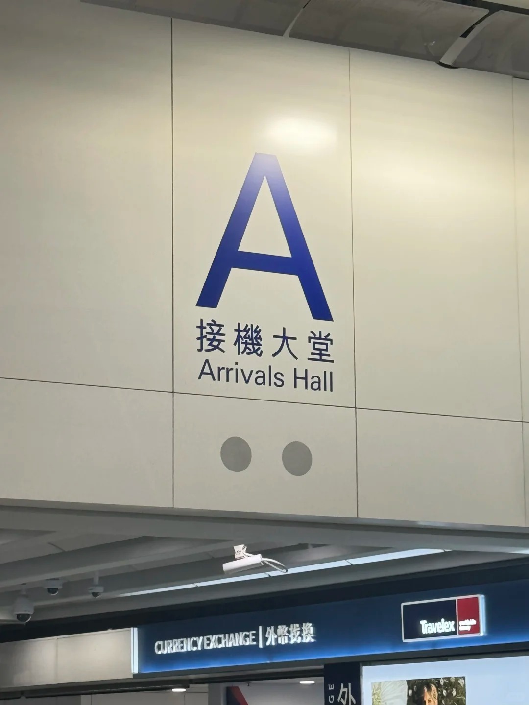 Arrivals Hall A sign at Hong Kong airport Terminal 1, with a Travelex currency-exchange counter below