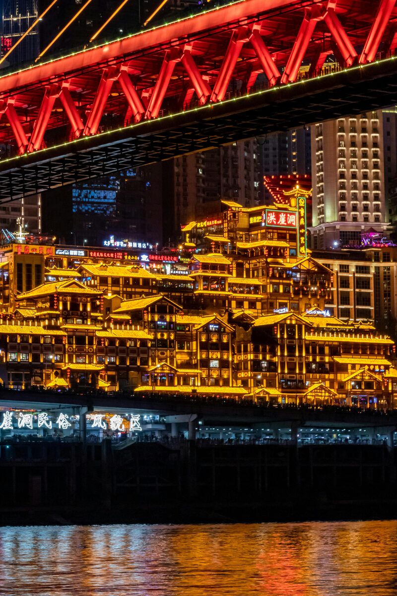 Hongyadong stilt-house complex lit up at night with neon reflections in the Jialing River, Chongqing.