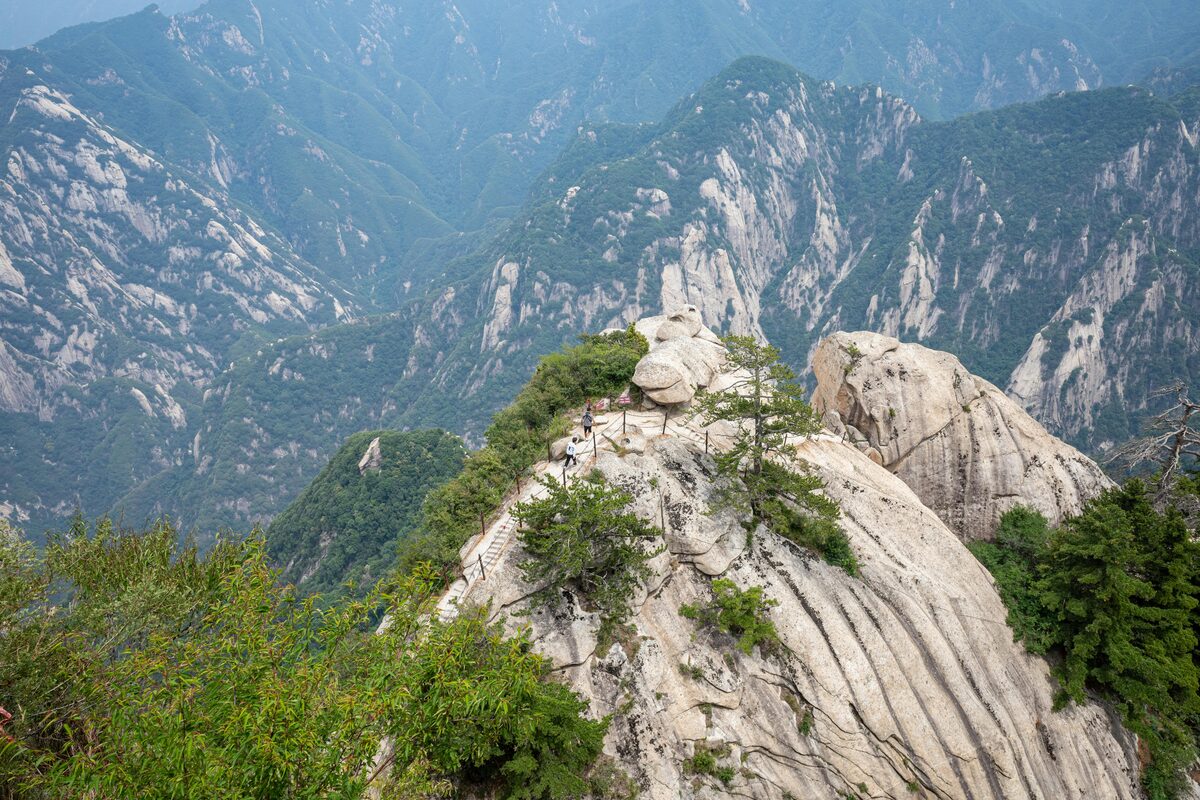 A narrow stone stairway climbing a granite ridge on Hua Shan, sheer drops on both sides into forested valleys.