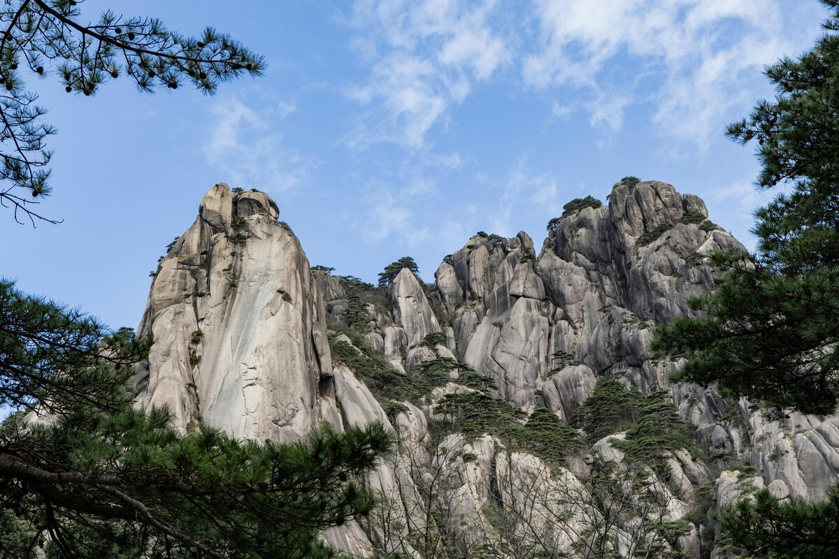 Jagged white granite spires of Hua Shan rising against a blue sky, framed by pine branches.