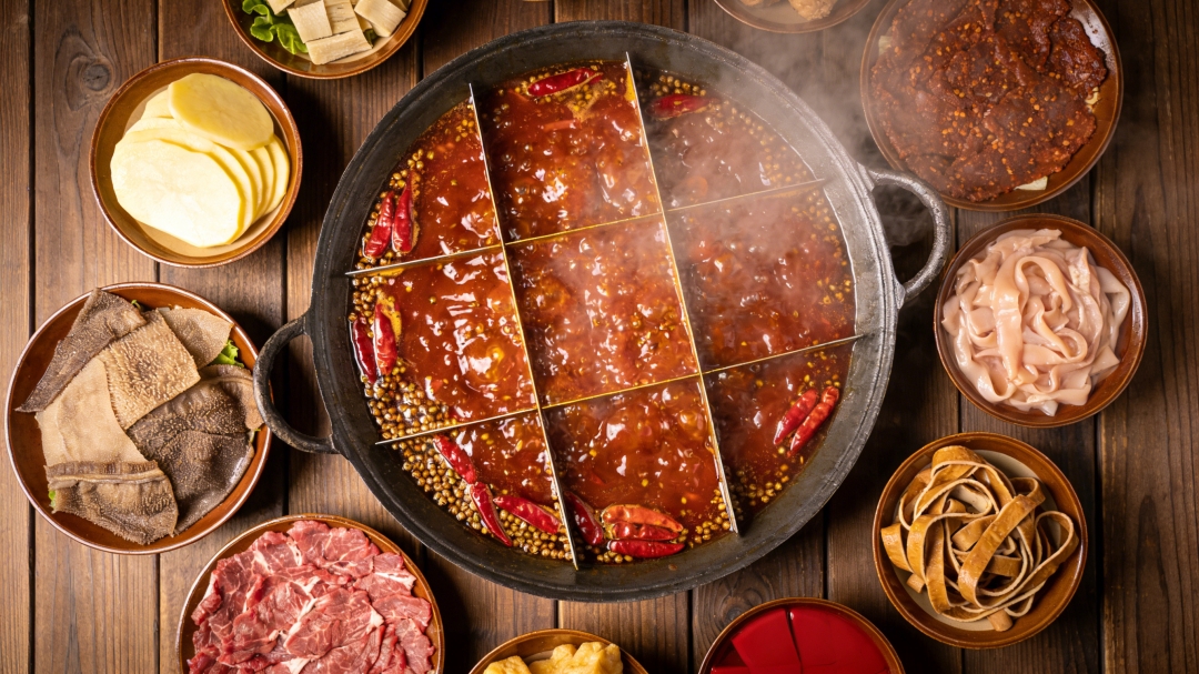 A nine-grid (九宫格) Chongqing-style hot pot bubbling with mala broth, dried chilies and Sichuan peppercorns, ringed by classic dipping plates — tripe, beef, tofu skin, potato.