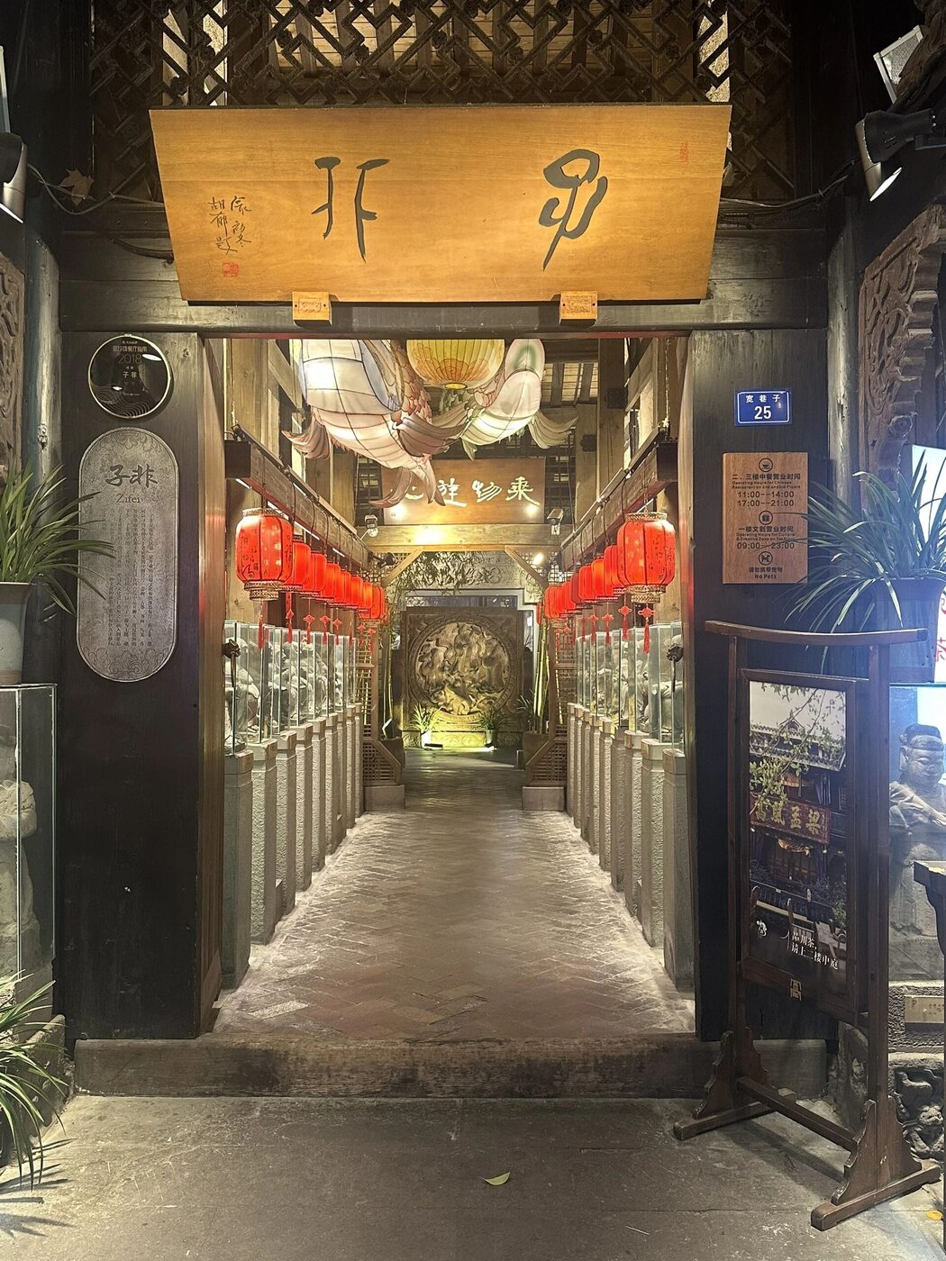 A lantern-lit courtyard entrance at Kuanzhai Alley after dark, red lanterns lining the stone passage with a carved-stone relief at the end, Chengdu.