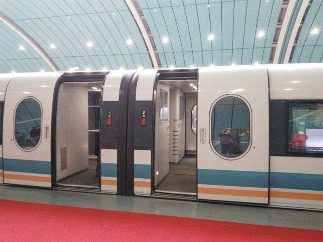 Shanghai Maglev cabin with doors open at a station, view into the interior showing seating, the corridor between rows, and the wide doorway used for boarding