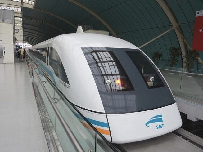 Shanghai Maglev train stopped at Longyang Road platform — full front quarter view showing the SMT logo, orange and turquoise stripes on white body, distinctive bullet-shaped nose