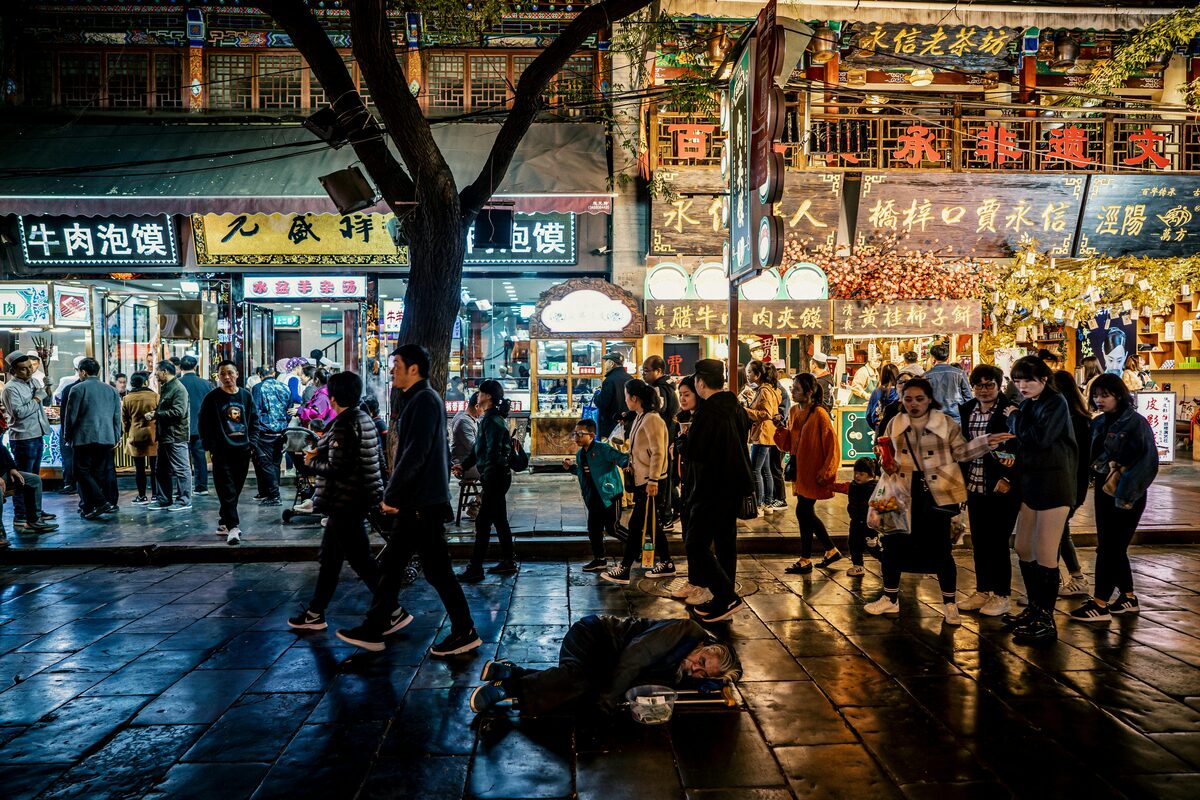 Crowds on Beiyuanmen food street in Xi'an's Muslim Quarter at night, lit shopfronts advertising beef paomo.