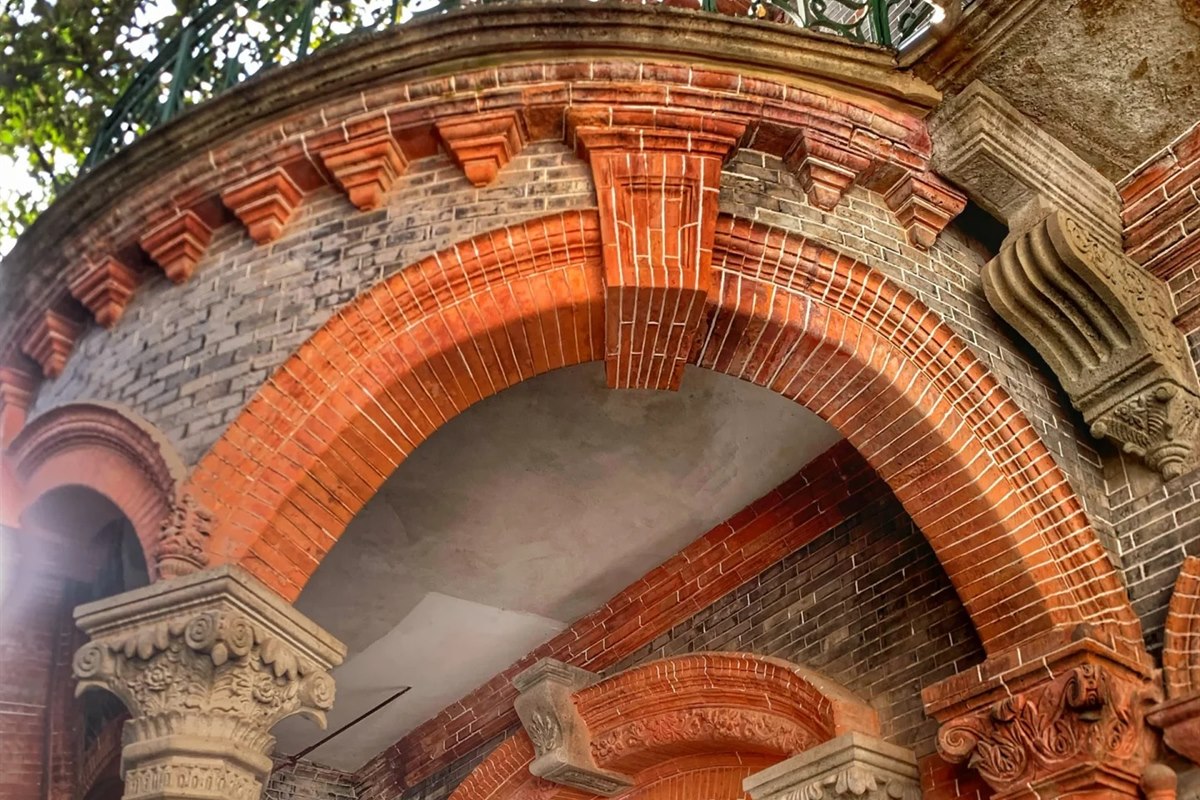 A two-storey arcade in a Nanxun merchant mansion: bright red brick arches springing from carved pale-stone Corinthian columns, with grey brick infill behind and a fanlight window over the doorway.