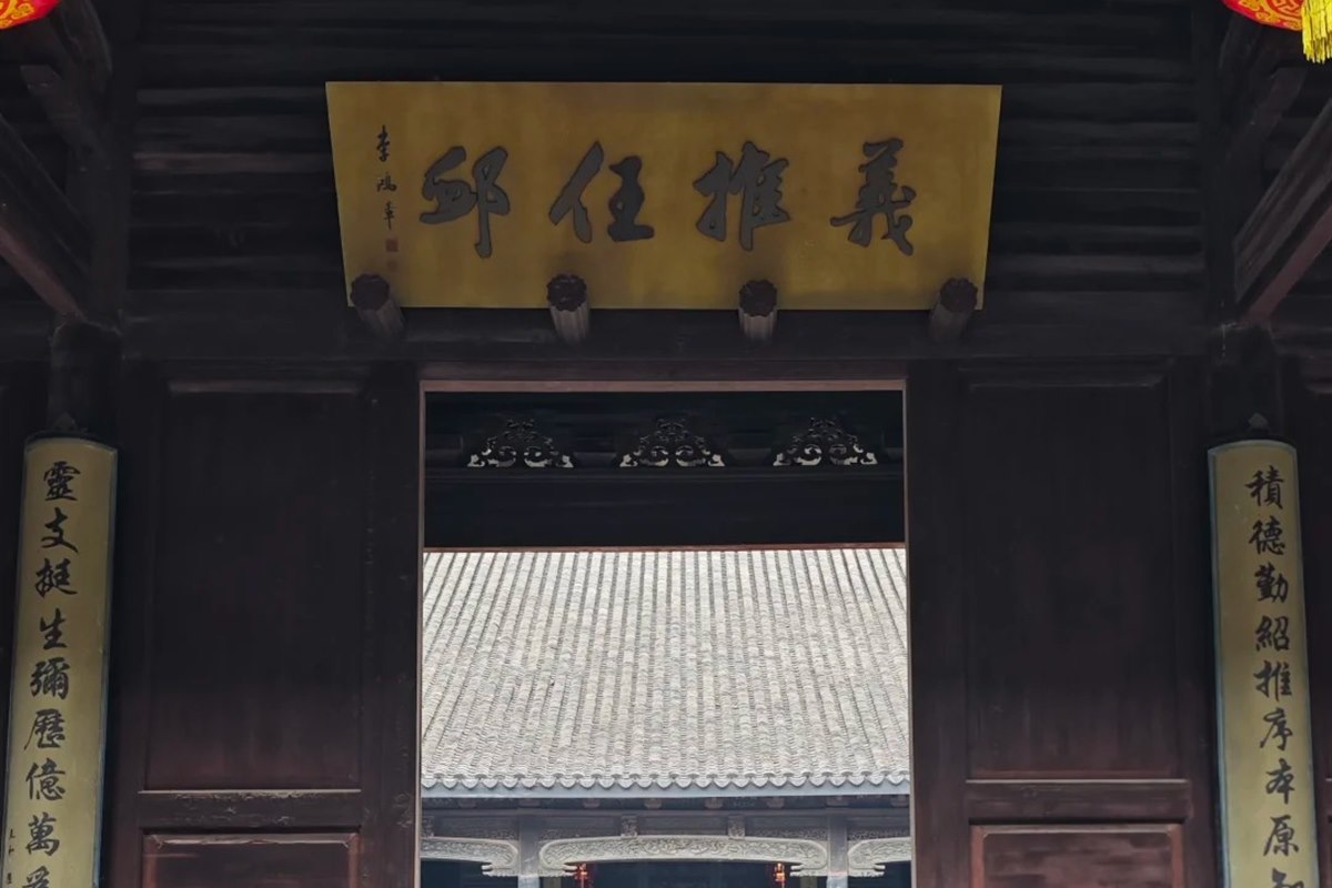 Looking through the open doors of the Liu family temple in Nanxun: a gilded board reading Yi Tui Ren Xu hangs over the entrance between two vertical inscribed panels, with a bronze censer and a tiled hall beyond in the courtyard.