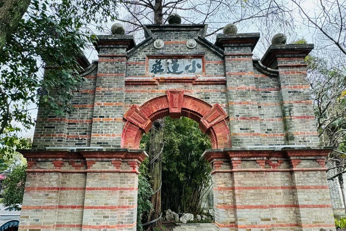 The gateway to the Xiaolianzhuang garden in Nanxun: a grey brick screen wall banded with red brick, pierced by a Western-style round arch, with a stone plaque reading Xiaolianzhuang set above it and bamboo visible through the opening.