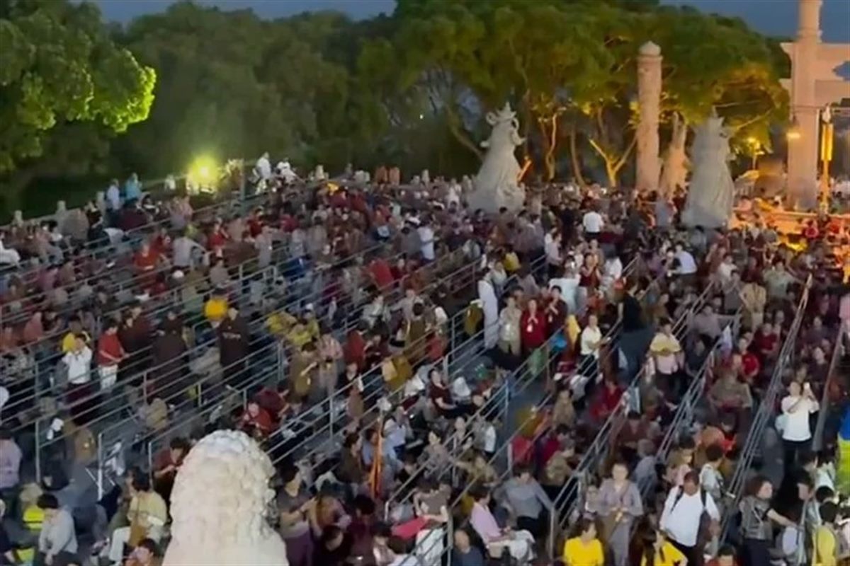 Dense crowds filling tiered steps and terraces on Putuoshan at dusk during a Guanyin festival, with stone carvings and lit trees behind them and the sea beyond.