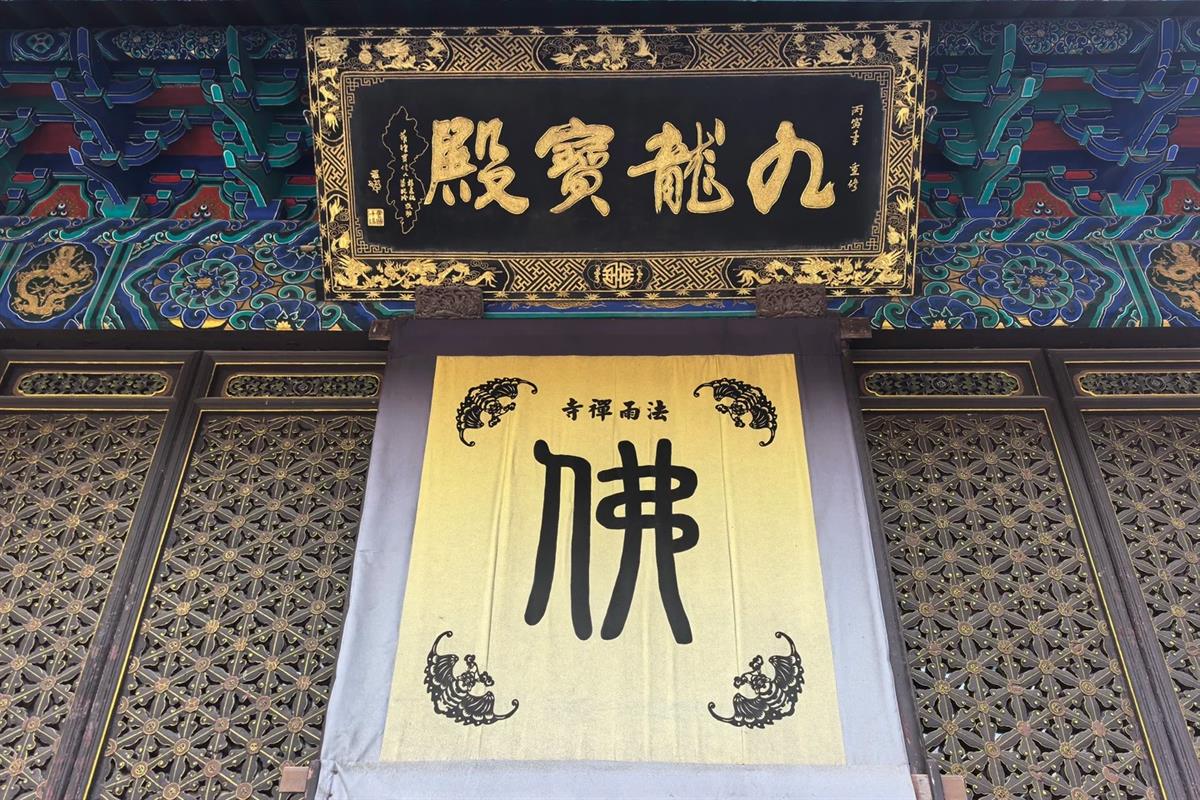 The Nine Dragon Hall at Fayu Temple: a black lacquered plaque with gold characters set into painted blue-and-green bracketing, above a yellow cloth banner bearing a single large character for Buddha.