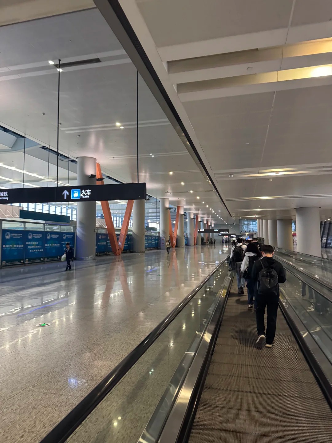 Travelator inside the Hongqiao hub with travellers and luggage heading toward the Train sign