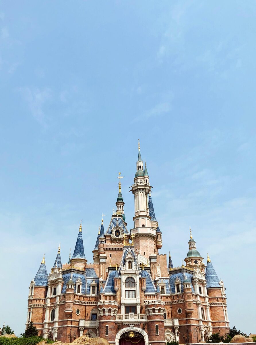 The Enchanted Storybook Castle at Shanghai Disneyland against a clear sky, showing its blue spires and stonework.