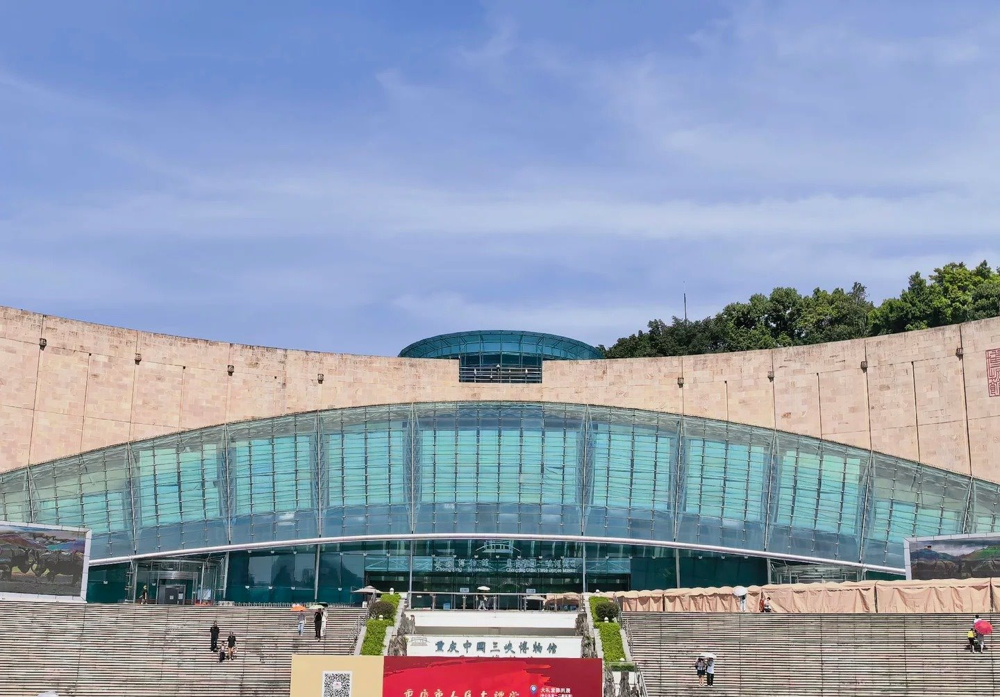 The museum's curved stone facade and glass frontage seen across the steps, with a freestanding board in front carrying a QR code and the words 扫码购票参观大礼堂 beside a red banner for the Great Hall of the People exhibition.