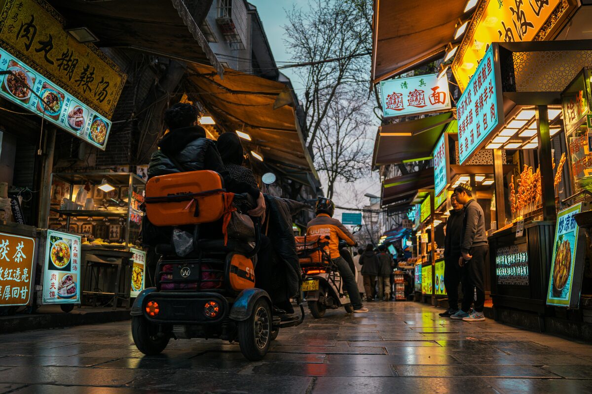 A narrow lane of glowing food stalls at dusk in Xi'an's Muslim Quarter, hand-written menu boards lining both sides.