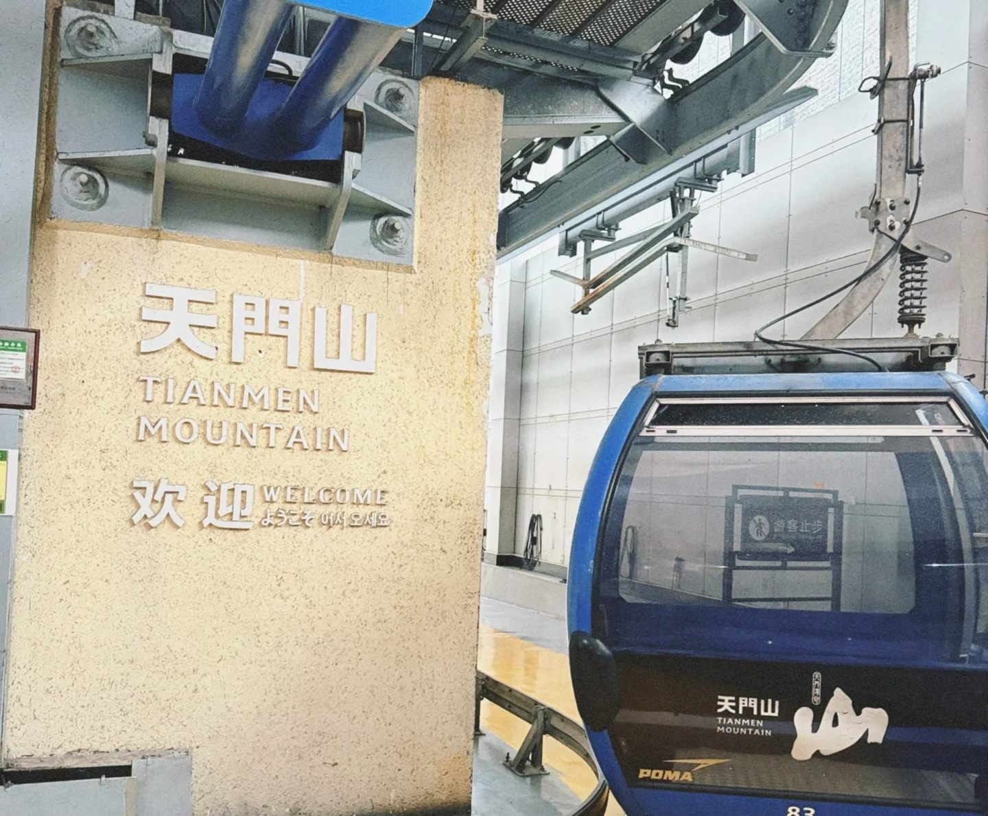The Tianmen Mountain cableway boarding hall, signed 天門山 TIANMEN MOUNTAIN, with a blue gondola on the turntable.