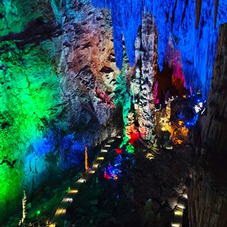A large chamber inside Furong Cave lit in green, blue and red, with a lit walkway threading between stalagmite columns.