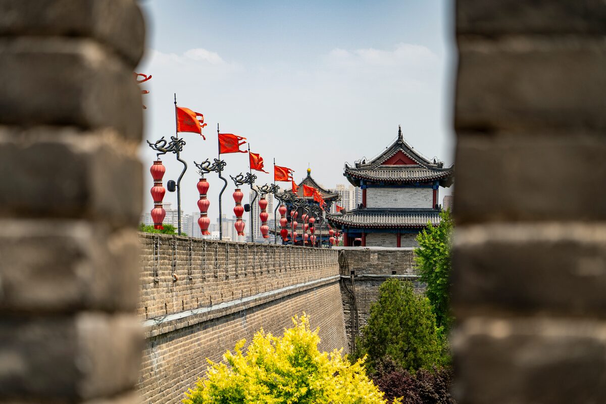View along the Xi'an City Wall walkway framed by a crenellation, red lanterns and flags lining the rampart toward a corner tower.